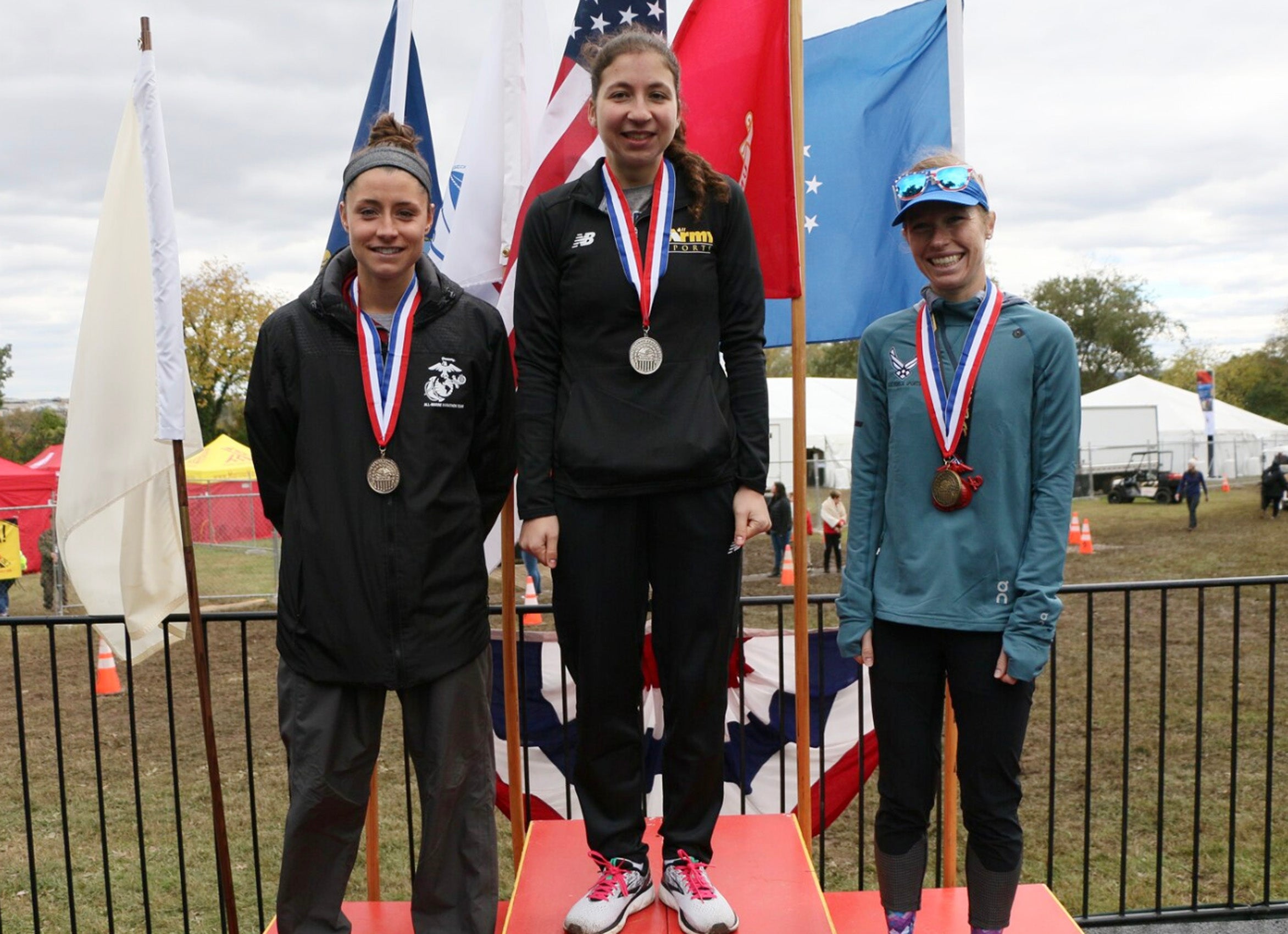 Three women posting on a winners platform wearing medals after a race.